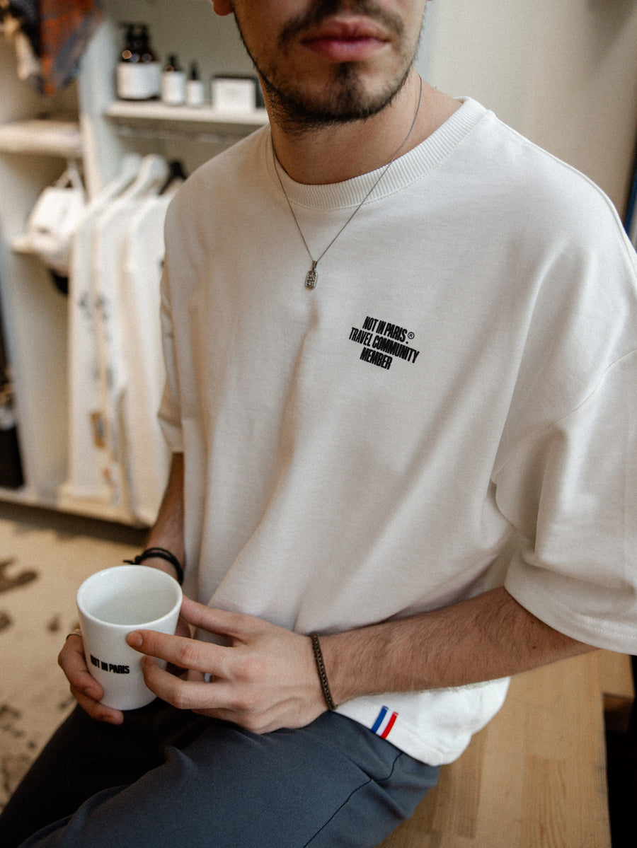 NOT IN PARIS À Travers l'Univers unisex tee — oversized front view with the chest print, holding a Not in Paris cup